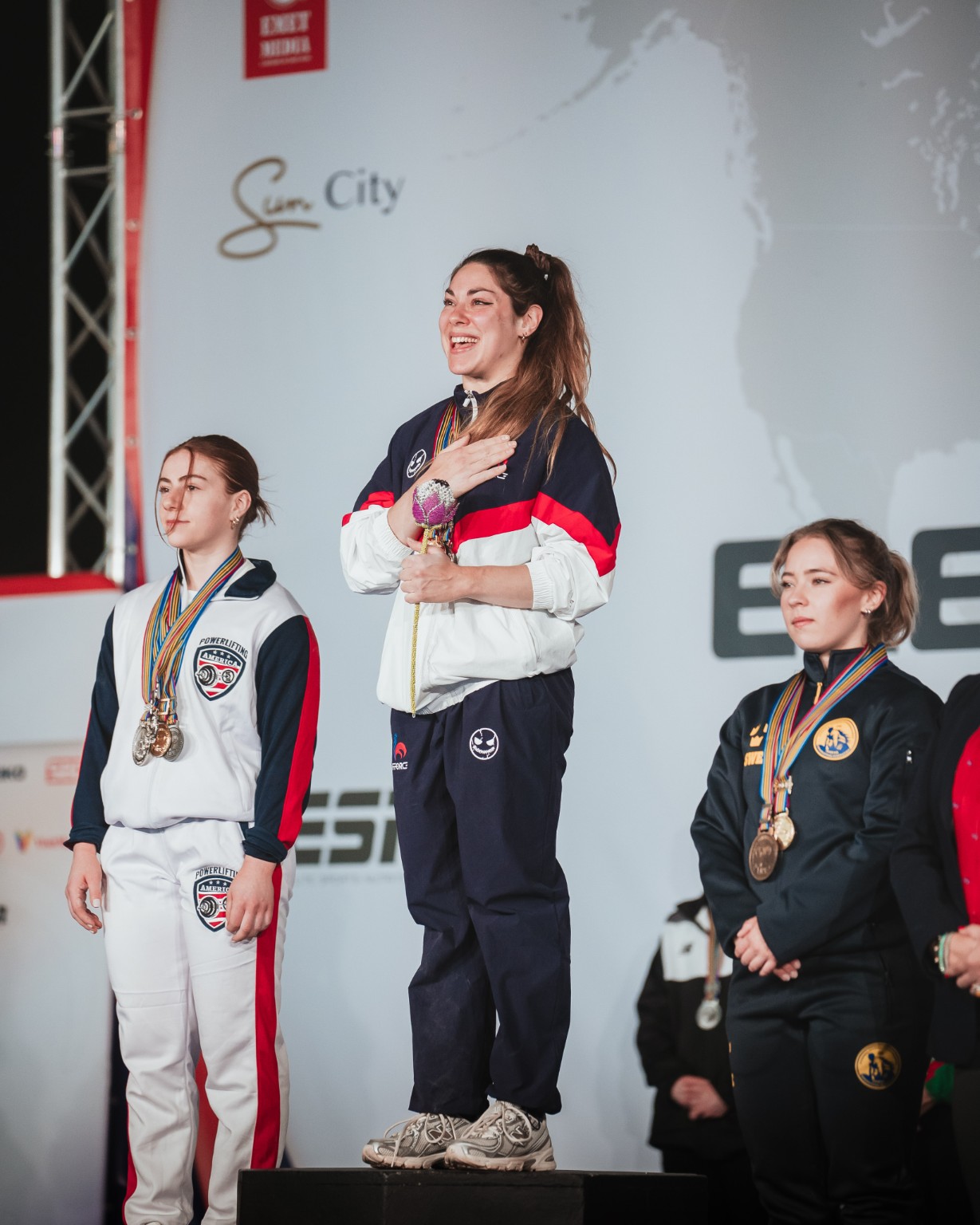 Eva Infantino souriante sur la première marche du podium des Mondiaux juniors, en tenue de l’équipe de France, médailles au cou et main sur le cœur